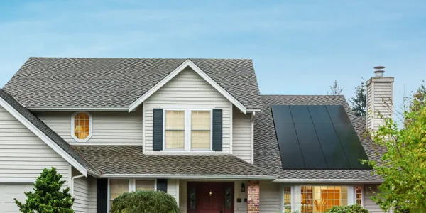 A house with white siding, gray shingles, and a solar panel with a blue sky in the background