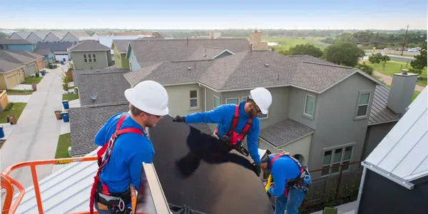 Three solar installation technicians carry a panel on the roof of a home in a neighborhood