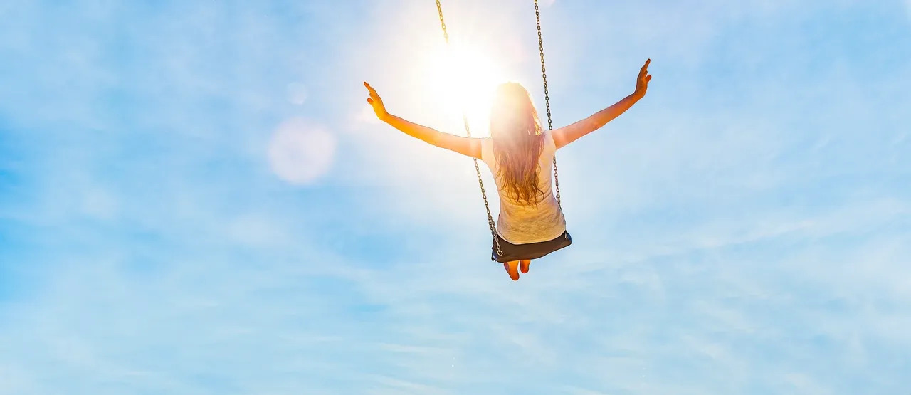 A young woman swinging on a swing with the sunlight outlining her